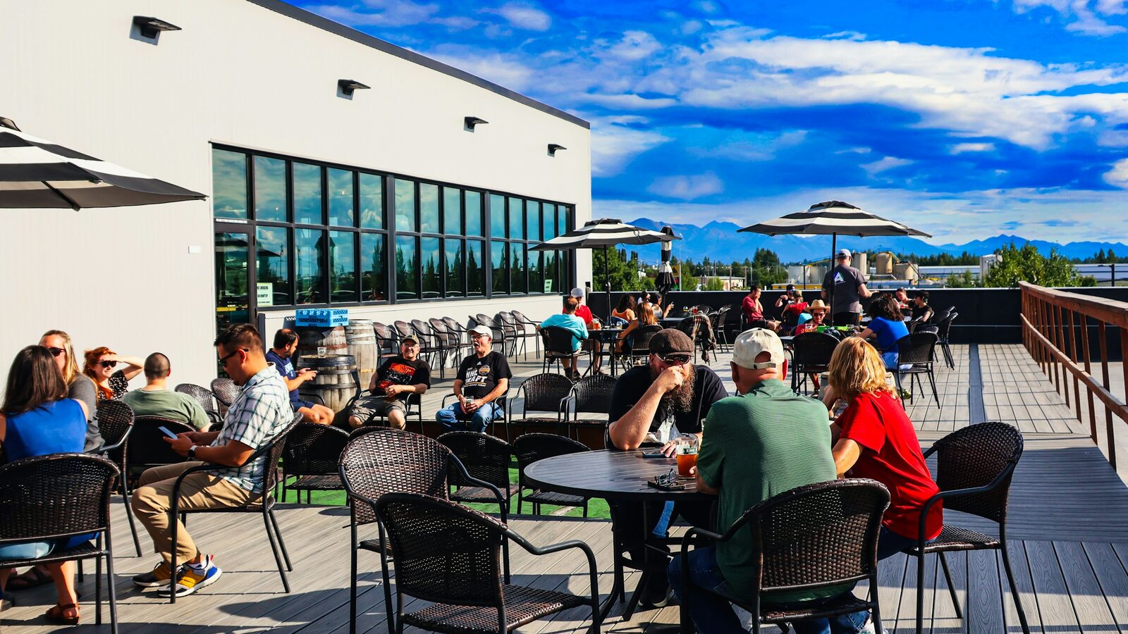 People sitting at tables on a sunny rooftop terrace under a blue sky, with mountains in the distance